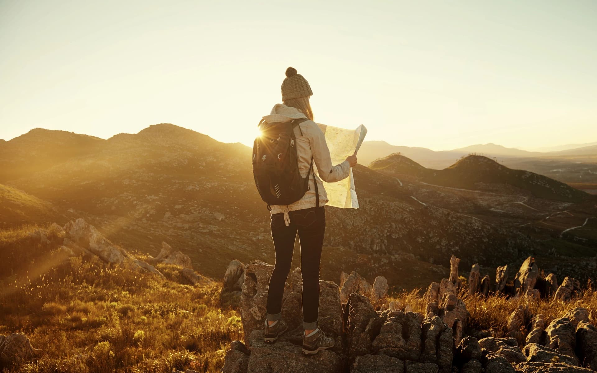 A hiker pausing at sunrise to read a map on a mountain ridge